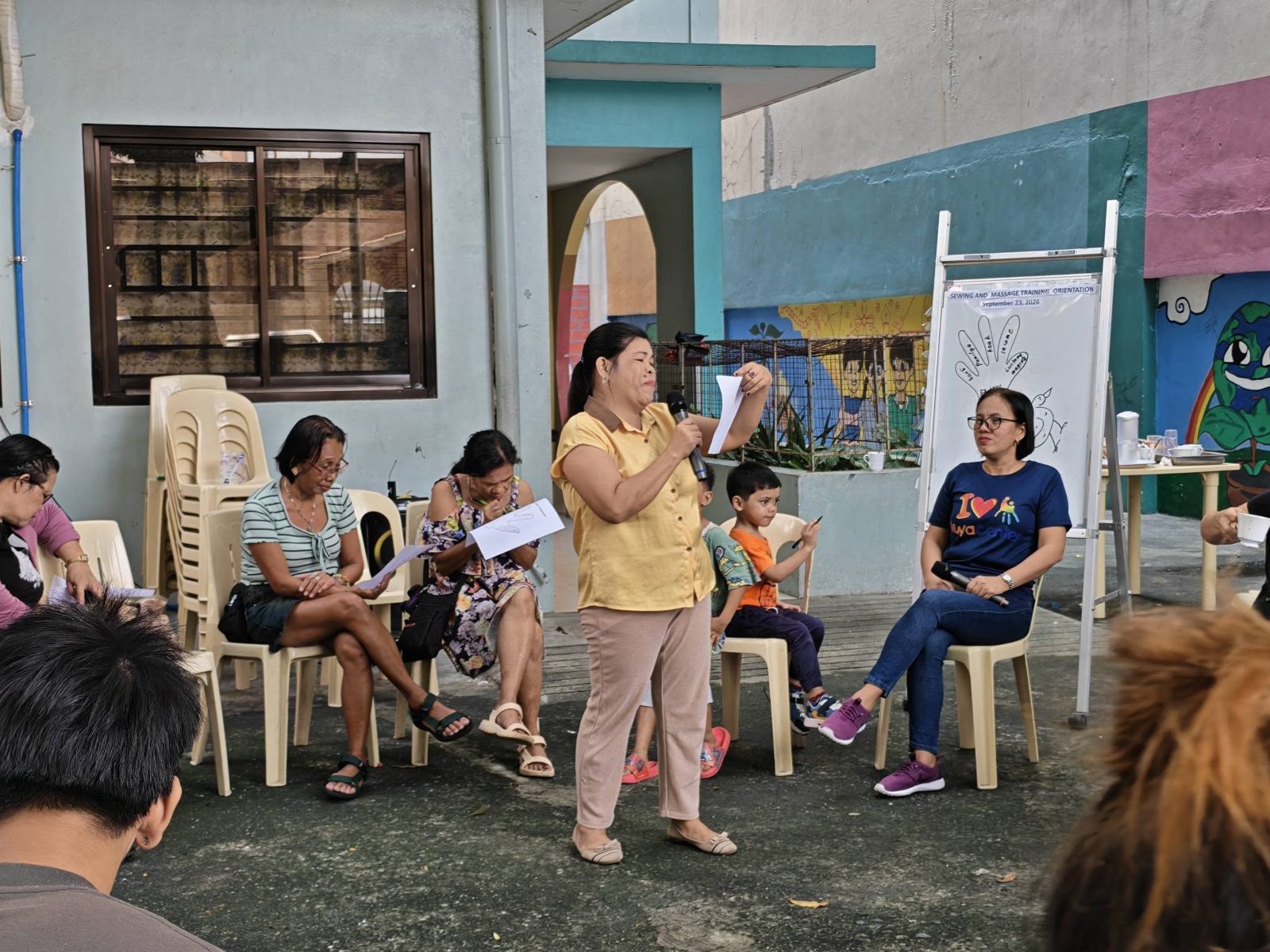 A parent speaking with a microphone during a group session in the Kuya Center courtyard