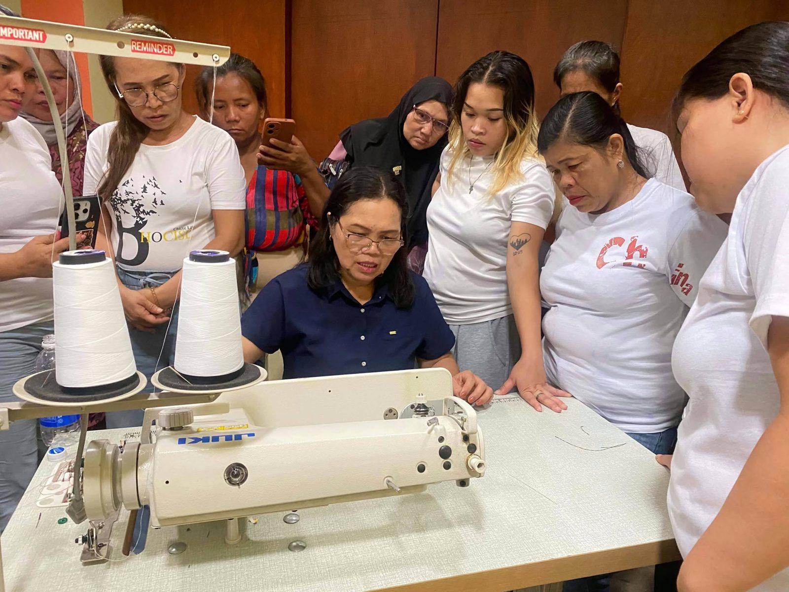 Parents gathered around a trainer demonstrating an industrial sewing machine